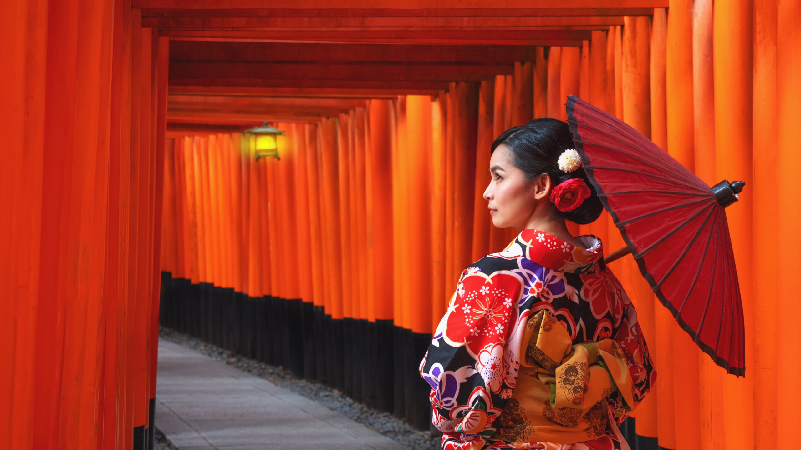 Vrouw in traditionele kleding in de rode torii-poorten van het Fushimi Inari-heiligdom in Kyoto