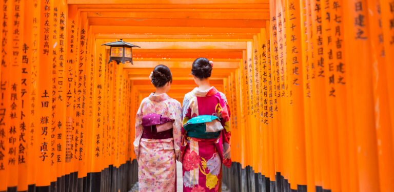 Twee geisha vrouwen lopen door de rode torii-poorten van het Fushimi Inari-taisha heiligdom in Kyoto