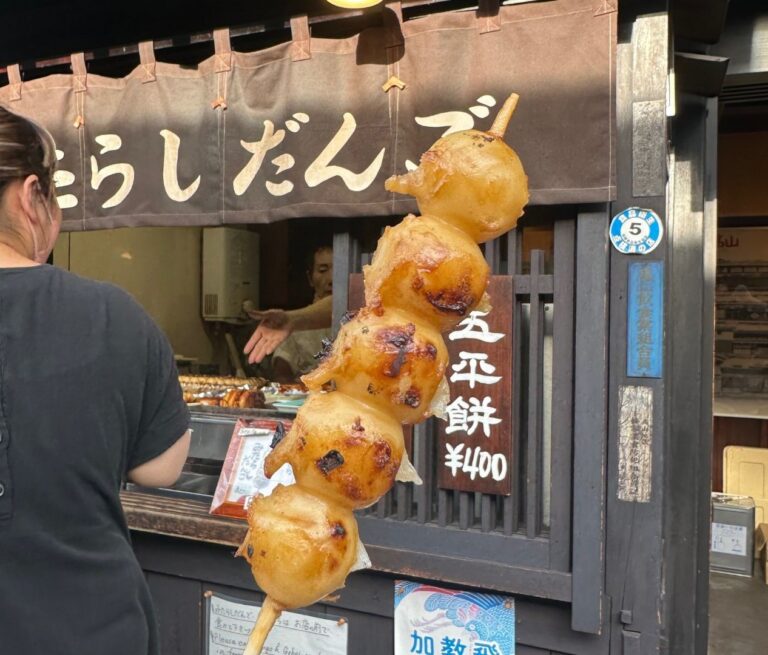 Een Mitarashi dango spies, omhooggehouden voor marktkraam, een populaire Japanse straatsnack bestaande uit rijstknoedels