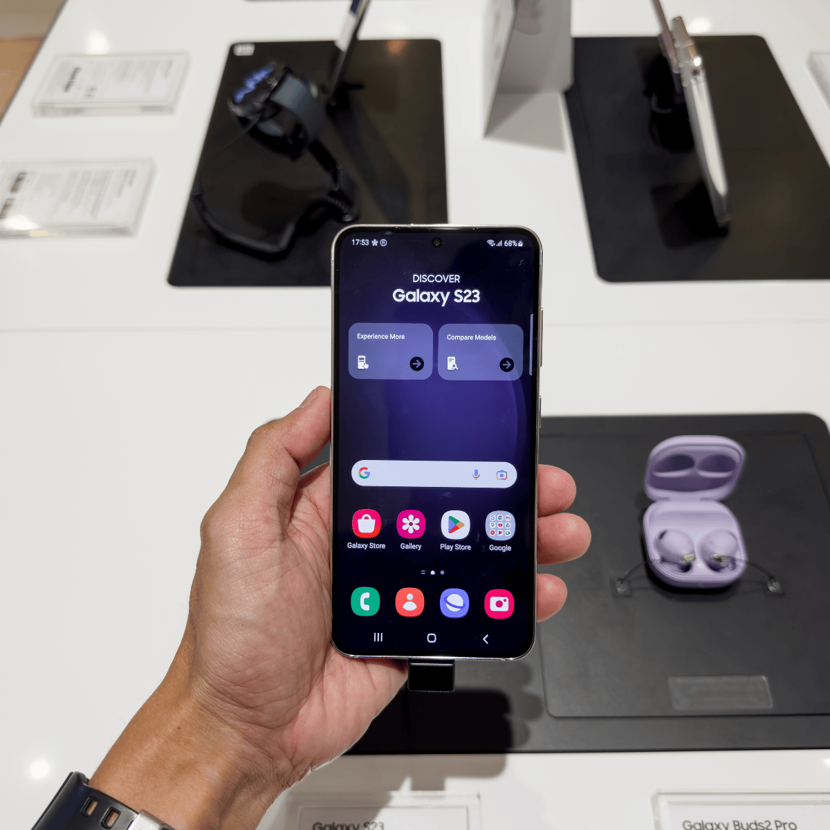 Téléphone Samsung S23 posé sur un support, avec ses caractéristiques techniques visibles en arrière-plan.