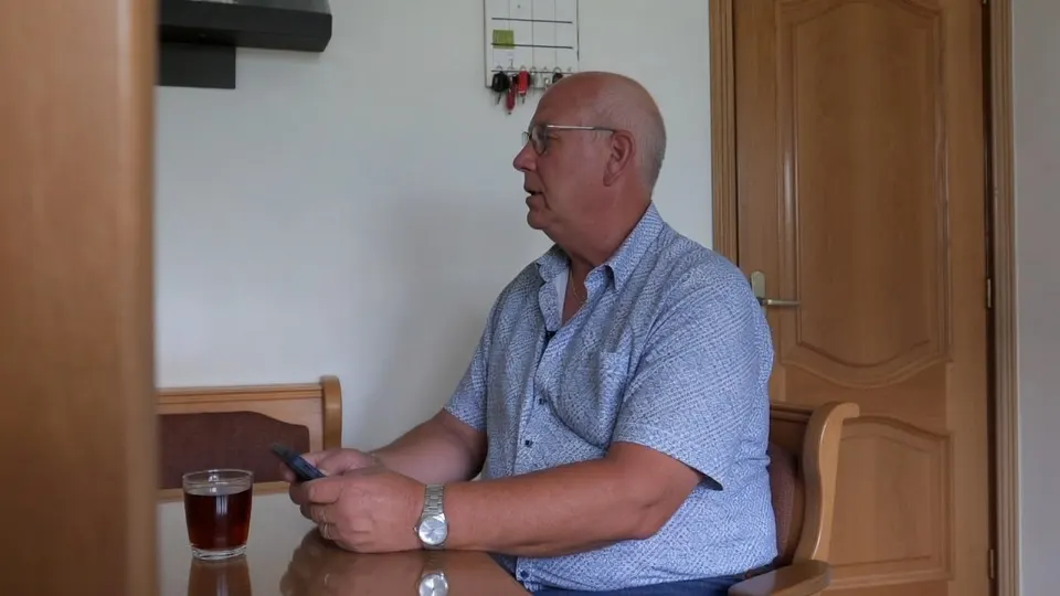 Koos de Visser uit Moerdijk zit thuis met zijn telefoon en een glas drinken