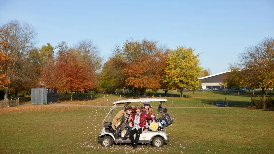 Leden van carnavalsband Kapotte Kachels rijden in een golfkar over een grasveld