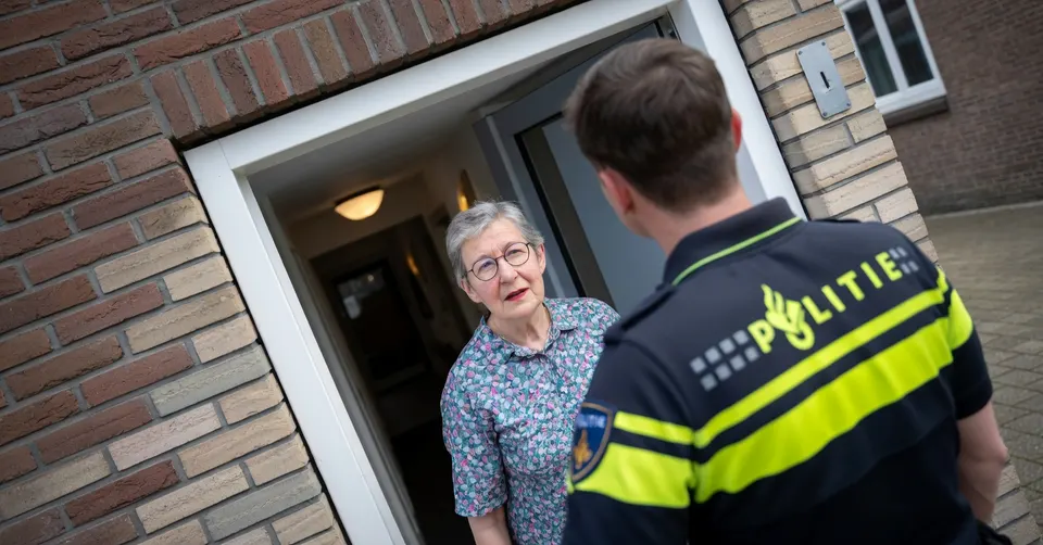 Een politieagent spreekt een oudere vrouw aan bij de voordeur