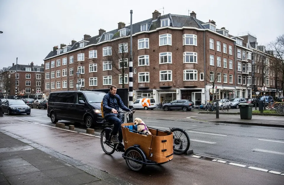Een ouder fietst met een kind in een bakfiets door een Amsterdamse straat