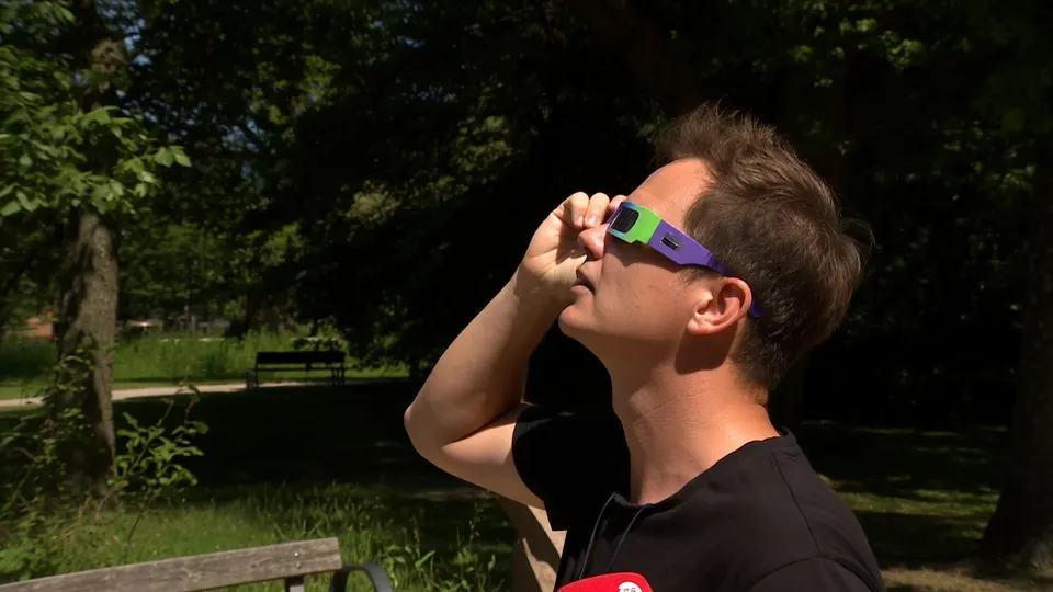 Man bekijkt de gedeeltelijke zonsverduistering door een eclipsbril