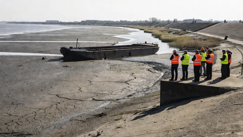 Inspecteurs bekijken een drooggevallen waterbekken met een verlaten boot