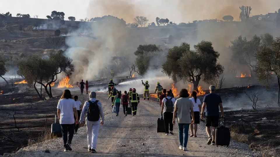 Geëvacueerde inwoners lopen langs brandweerlieden en bosbranden op het Griekse eiland Salamina