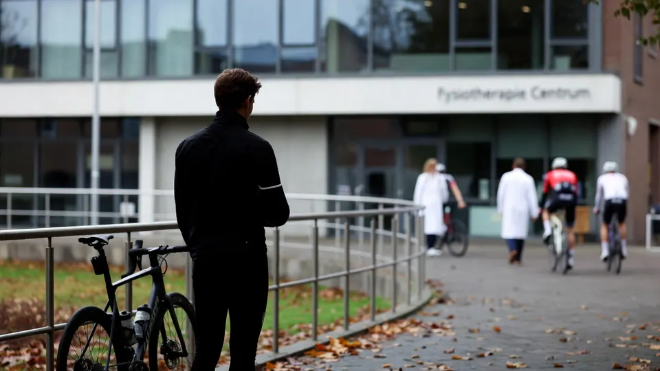 Een wielrenner staat met zijn fiets voor een fysiotherapiecentrum