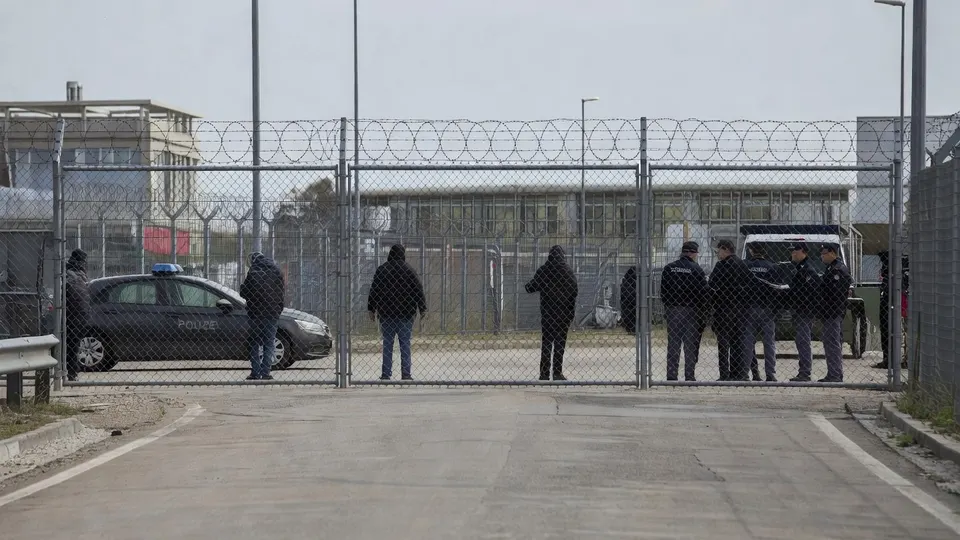 Politie en andere betrokkenen staan bij de ingang van een omheind terrein