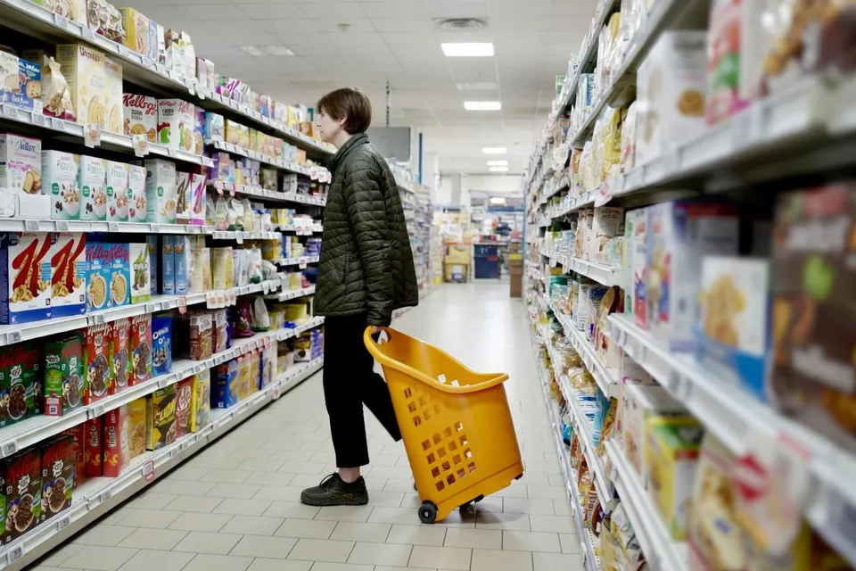 Consument met winkelmandje in een supermarkt, tussen de schappen met levensmiddelen