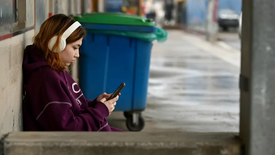 Tiener gebruikt een smartphone naast afvalcontainers