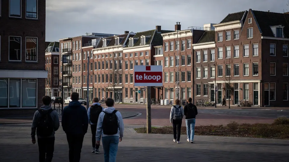 Jongeren lopen langs woningen met een bord waarop staat dat een huis te koop staat