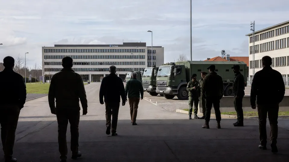 Militairen lopen langs legertrucks op een terrein van Defensie