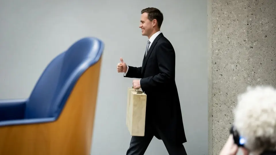 Een man loopt met een tas langs een blauwe stoel in de Tweede Kamer