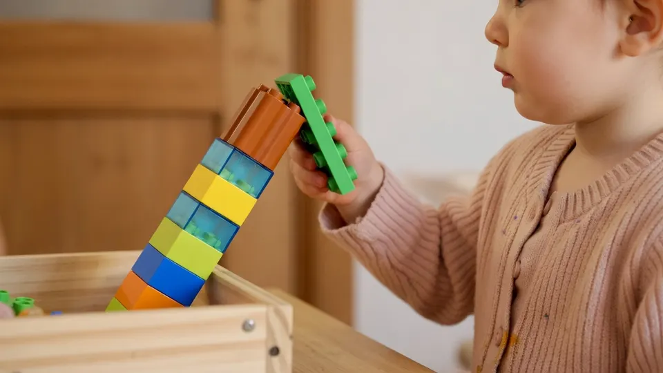 Een kind speelt met houten blokken, terwijl de kinderopvangsector zorgen houdt over bijna gratis opvang