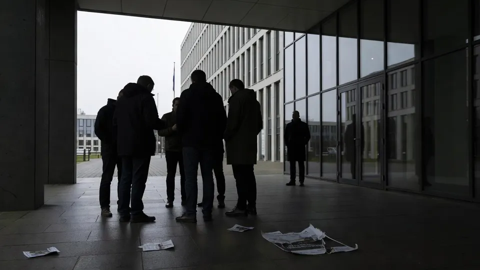 Mensen lopen langs een kantoorgebouw, terwijl folders op de grond liggen