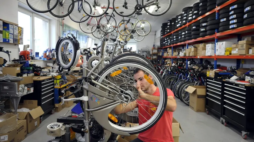Medewerker repareert een fiets in een winkel vol fietsen en fietsbanden
