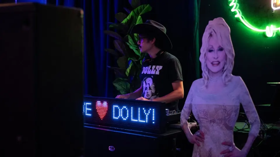 Bezoeker met Dolly Parton-shirt en cowboyhoed naast een levensgrote afbeelding van de zangeres