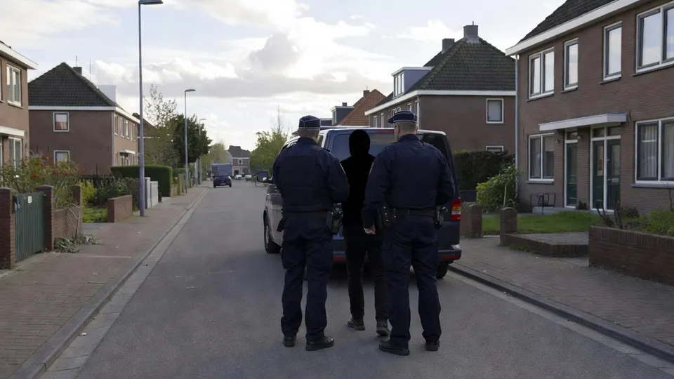 Agenten begeleiden een verdachte naar een politieauto