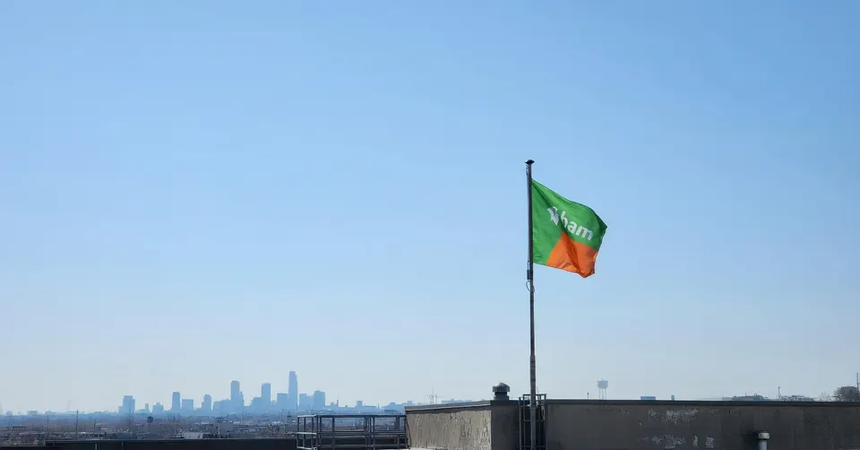 De vlag van infrastructuurbedrijf A.Hak wappert boven een dak, met een stads skyline op de achtergrond