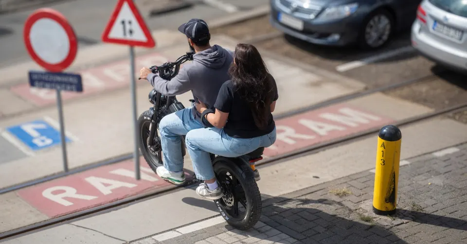 Twee mensen rijden op een fatbike langs verkeersborden en een fietspad