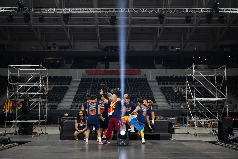 Een groep mensen staat samen op een podium in een lege sporthal