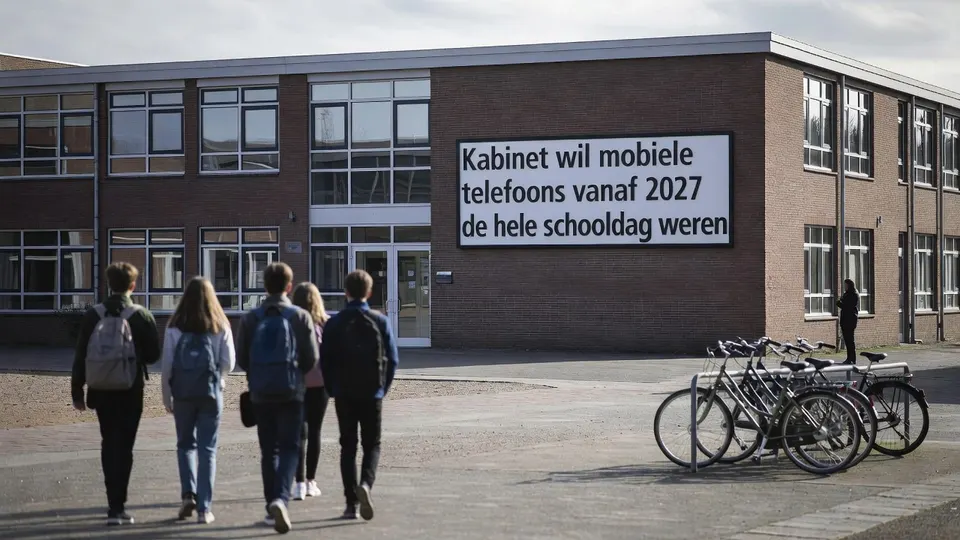 Leerlingen lopen het schoolplein op langs een bord over het voorgenomen verbod op mobiele telefoons