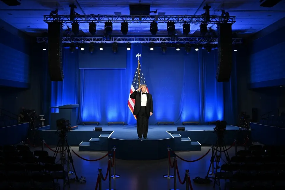 Donald Trump spreekt tijdens een bijeenkomst op een podium naast de Amerikaanse vlag