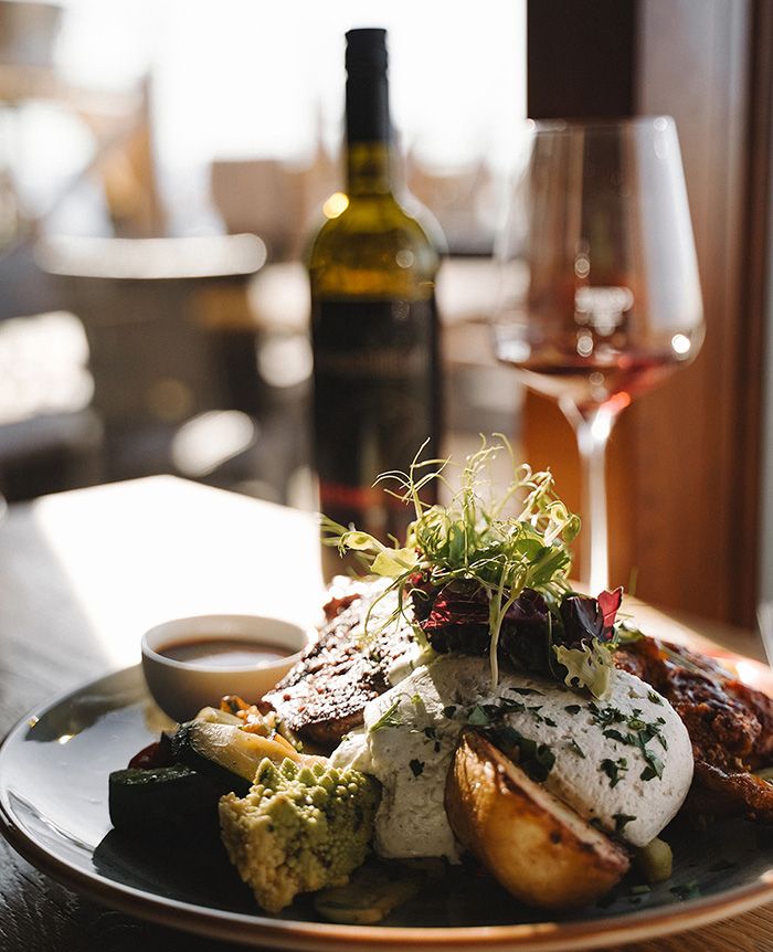 Teller mit gebratenem Fleisch, Kräuterquark, Gemüse und Kartoffelspalten, im Hintergrund Weinflasche und halb gefülltes Weinglas.