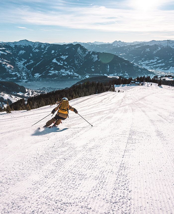 Skifahrer mit gelbem Rucksack fährt eine frisch präparierte Piste in den Bergen hinab.