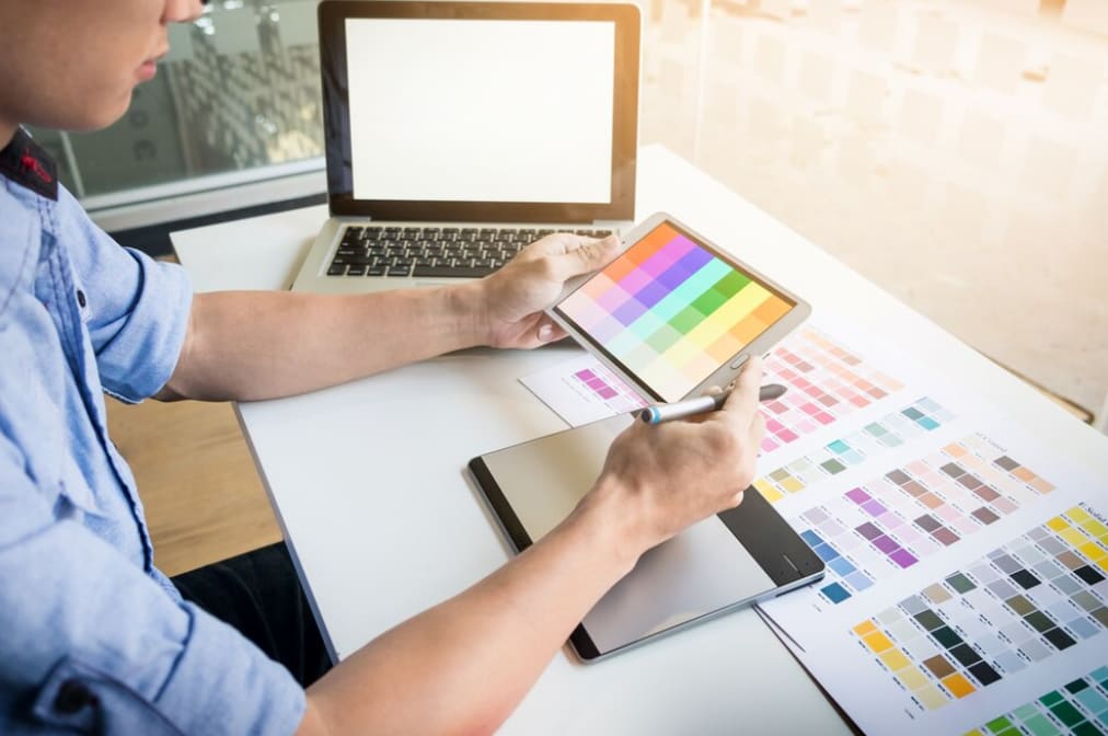 A person is selecting colors on a tablet with a color chart printout