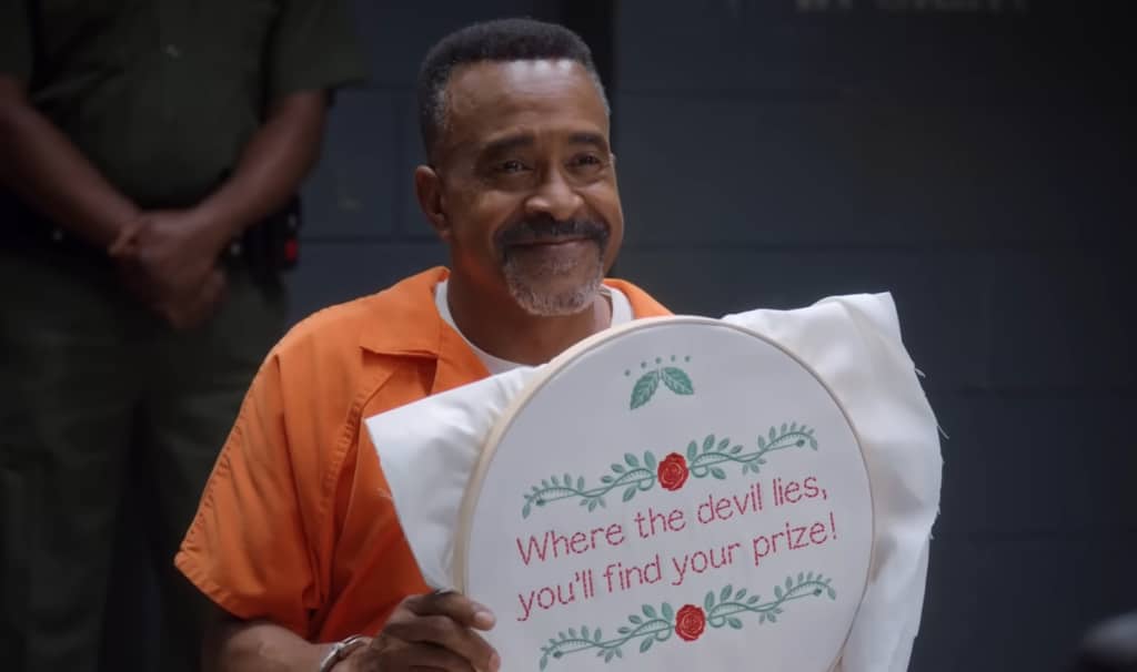 A smiling man in an orange jumpsuit holds an embroidered message