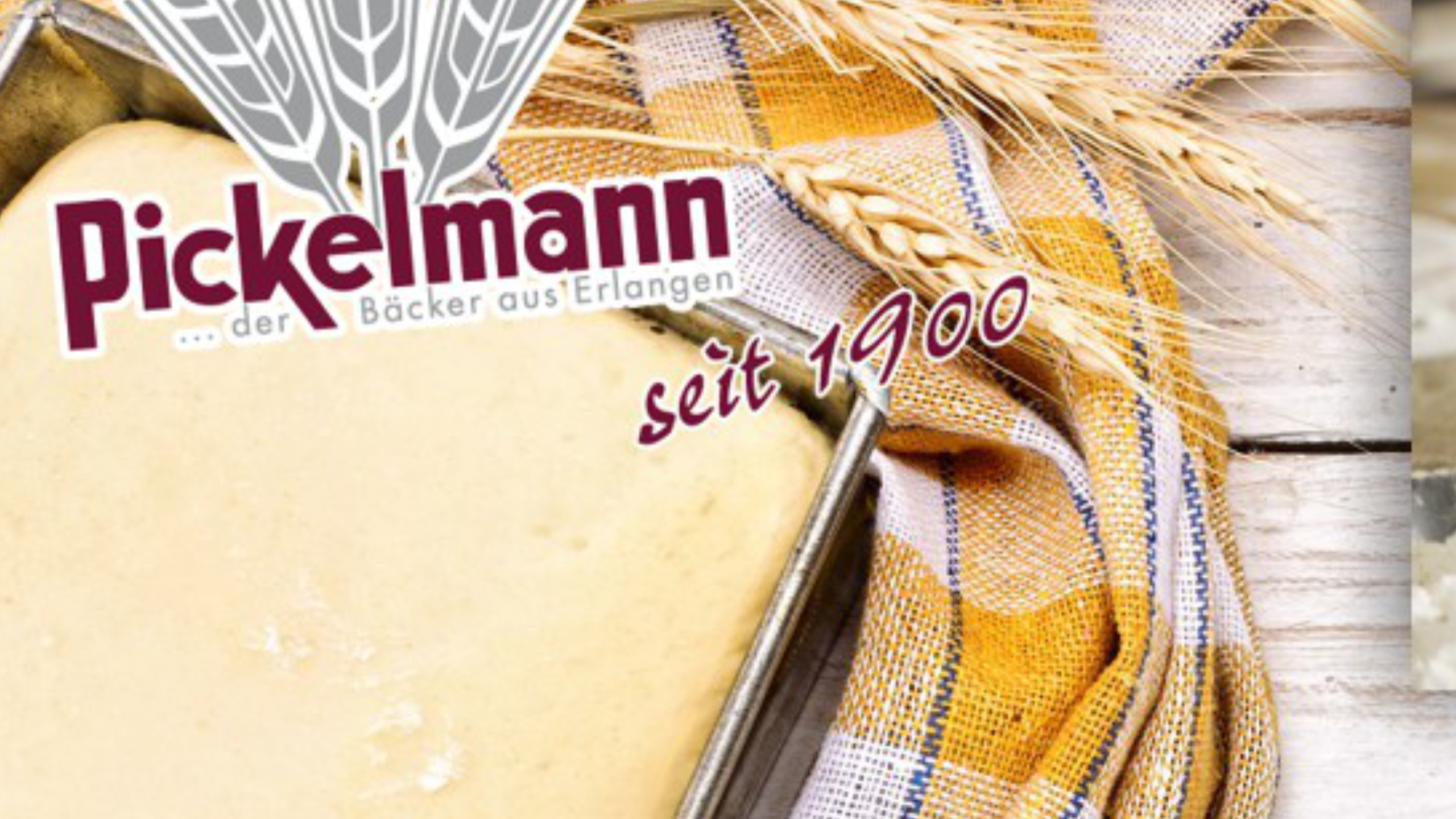 Werbebild für "Pickelmann, der Bäcker aus Erlangen seit 1900", zeigt rohen Teig in einer Backform, Getreideähren und ein gemustertes Tuch auf Holzuntergrund.
