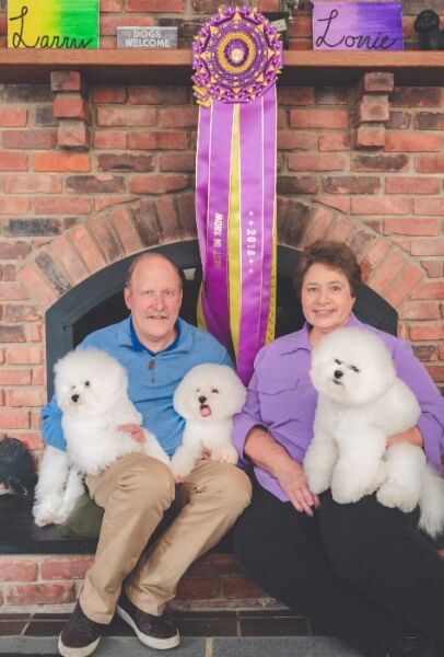 Lorrie Carlton & Larry Letsche DVM with their Bichons Frises sitting in their lap.