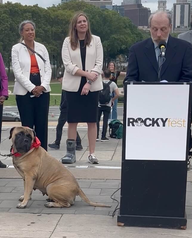 ROCKYFEST 2024 LAUNCH - Steve Griffith, Kennel Club of Philadelphia Director of Communications, details The National Dog Show’s involvement in RockyFest 2024 during the October press conference announcing RockyFest 2024 activities centering on the iconic movie, Rocky. Representing Rocky’s companion and training partner, Butkus, and the Bullmastiff breed is Wasabi, a member of the National Dog Show Therapy Dog Ambassador Team. Created by the Philadelphia Visitor Center Corp., RockyFest is an international tourist attraction featuring bus tours, film festivals, ice skating rink date nights, and the Southpaws Yappy Hour, Thursday, Dec. 5, on the Delaware River Waterfront. Photo Credit: Kathi Graham/National Dog Show