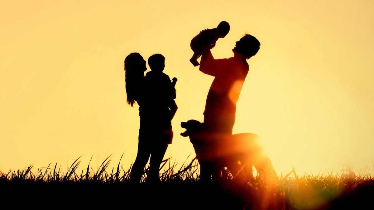 A silhouette of a happy family of four people, mother, father, baby, and child, and their dog in front of a sunsetting sky