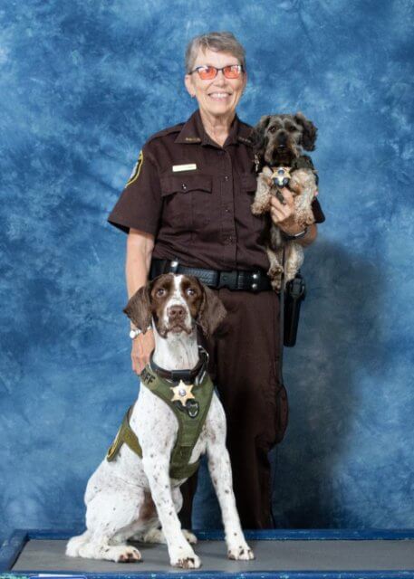 Sue Stejskal, wearing a police uniform is holding two dogs.