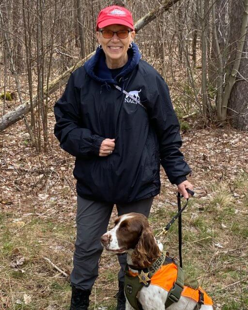 Sue Stejskal holding a dog on a leash in the woods.