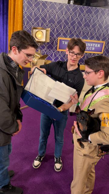 Gideon, Adam, and Hadrian open the trophy box backstage.