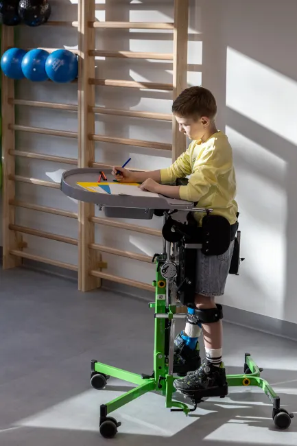 bērns sēž īpaši pielāgotā krēslā un zīmē