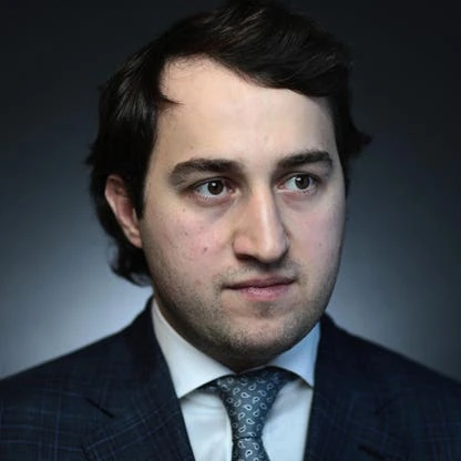 Portrait photo of Said Mikhailovich Gutseriev in a suit and tie against a dark background.