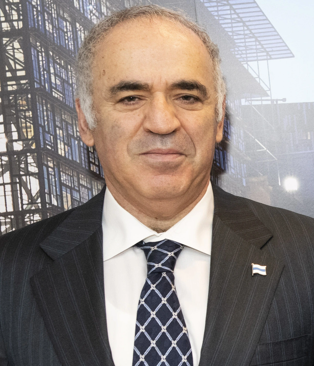 Garry Kasparov in a suit and tie, standing in front of an architectural backdrop