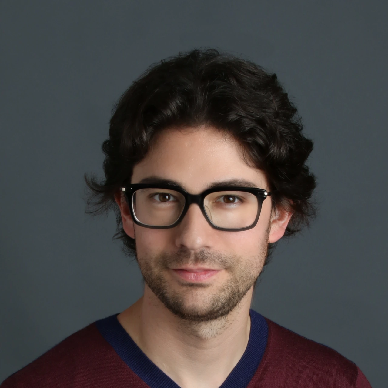 Portrait photo of Emmanuel Straschnov against a plain gray background, wearing glasses and a dark sweater.