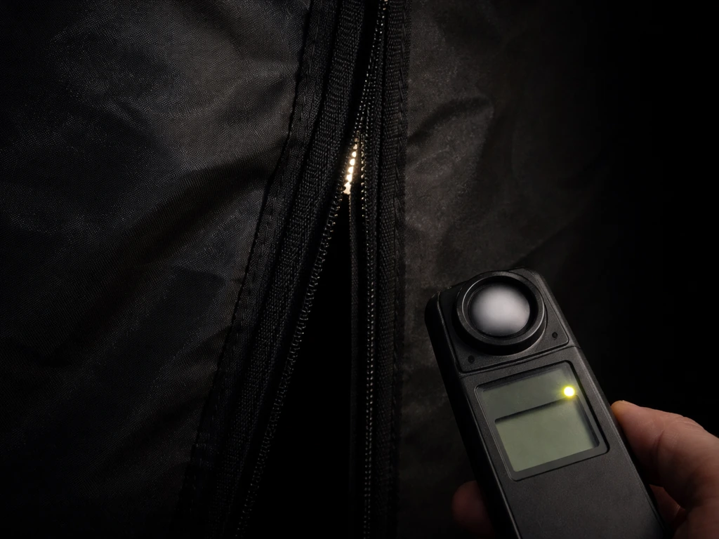 Close-up of a dark indoor grow tent zipper area with a small light meter checking for light leaks.