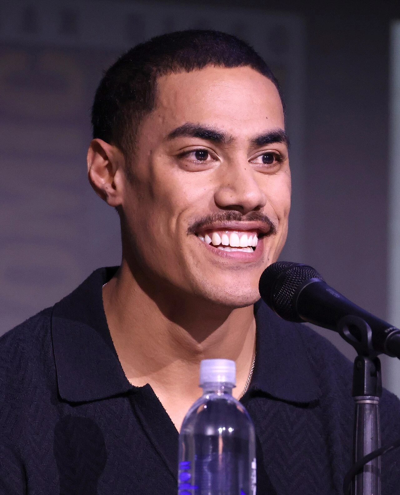 Portrait of Dimitrius Schuster-Koloamatangi speaking at a microphone
