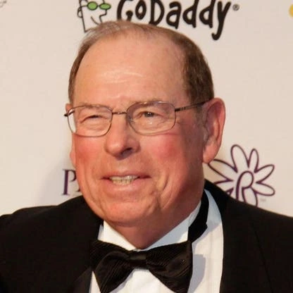 George Argyros Sr. in a tuxedo at an event, photographed against a branded backdrop.