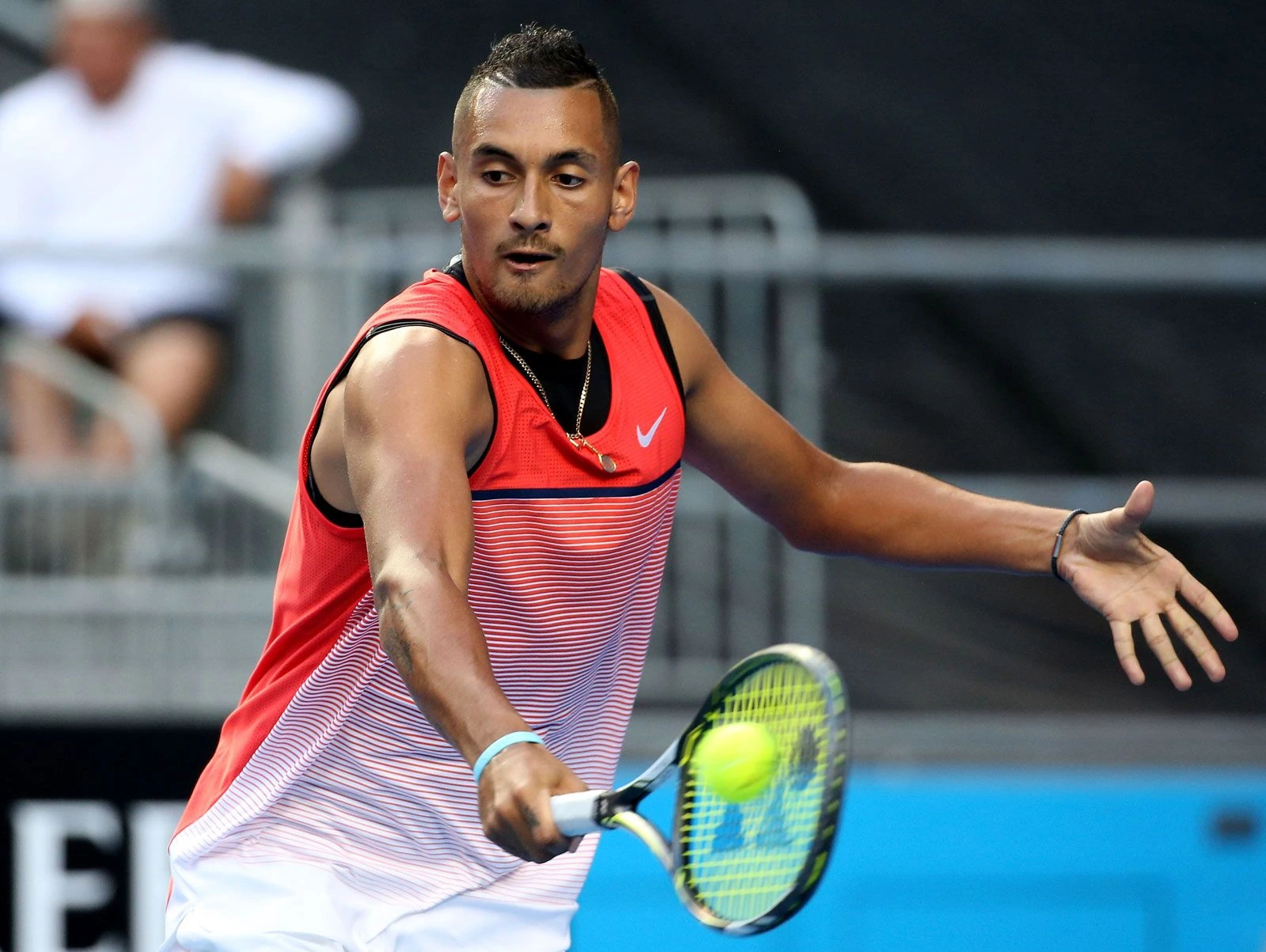 Nick Kyrgios playing tennis in a red sleeveless top, swinging a racket during a match.