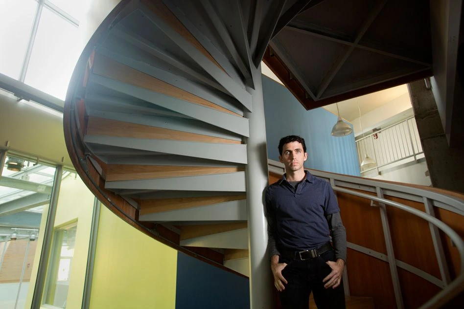 Manolis Kellis standing indoors beside a spiral staircase