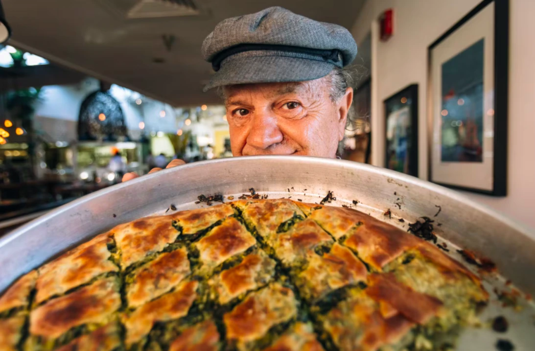 Giorgios Bakatsias holding a large tray of food in a restaurant kitchen or dining area