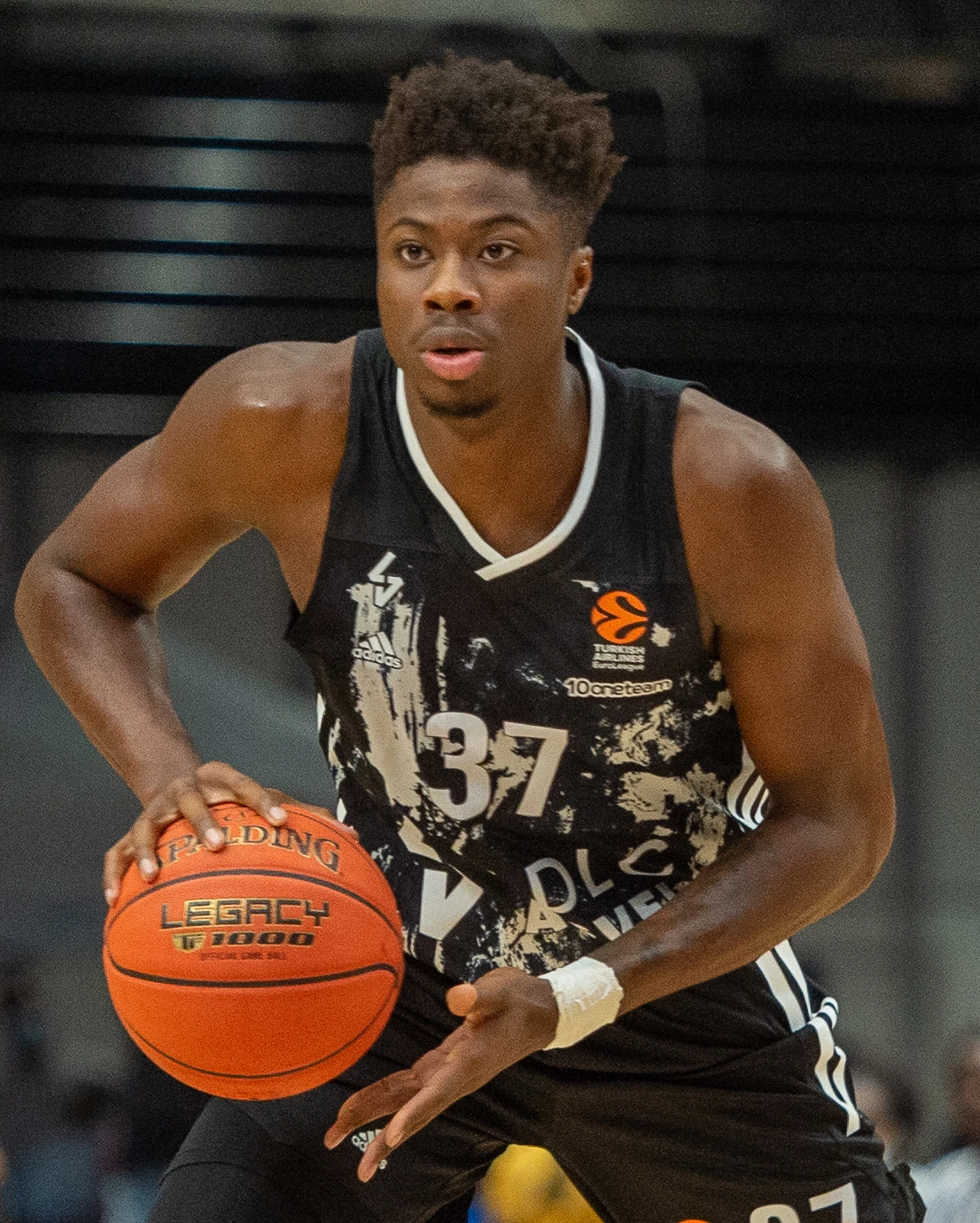 Kostas Antetokounmpo in a black basketball jersey dribbling during a game